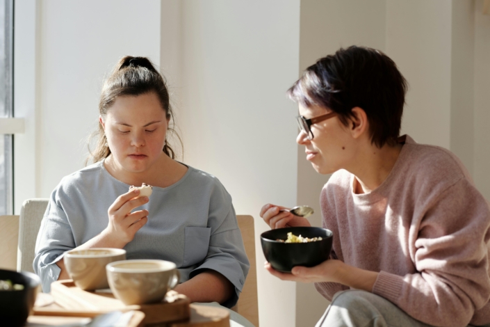 a support worker sitting with a young woman eating breakfast